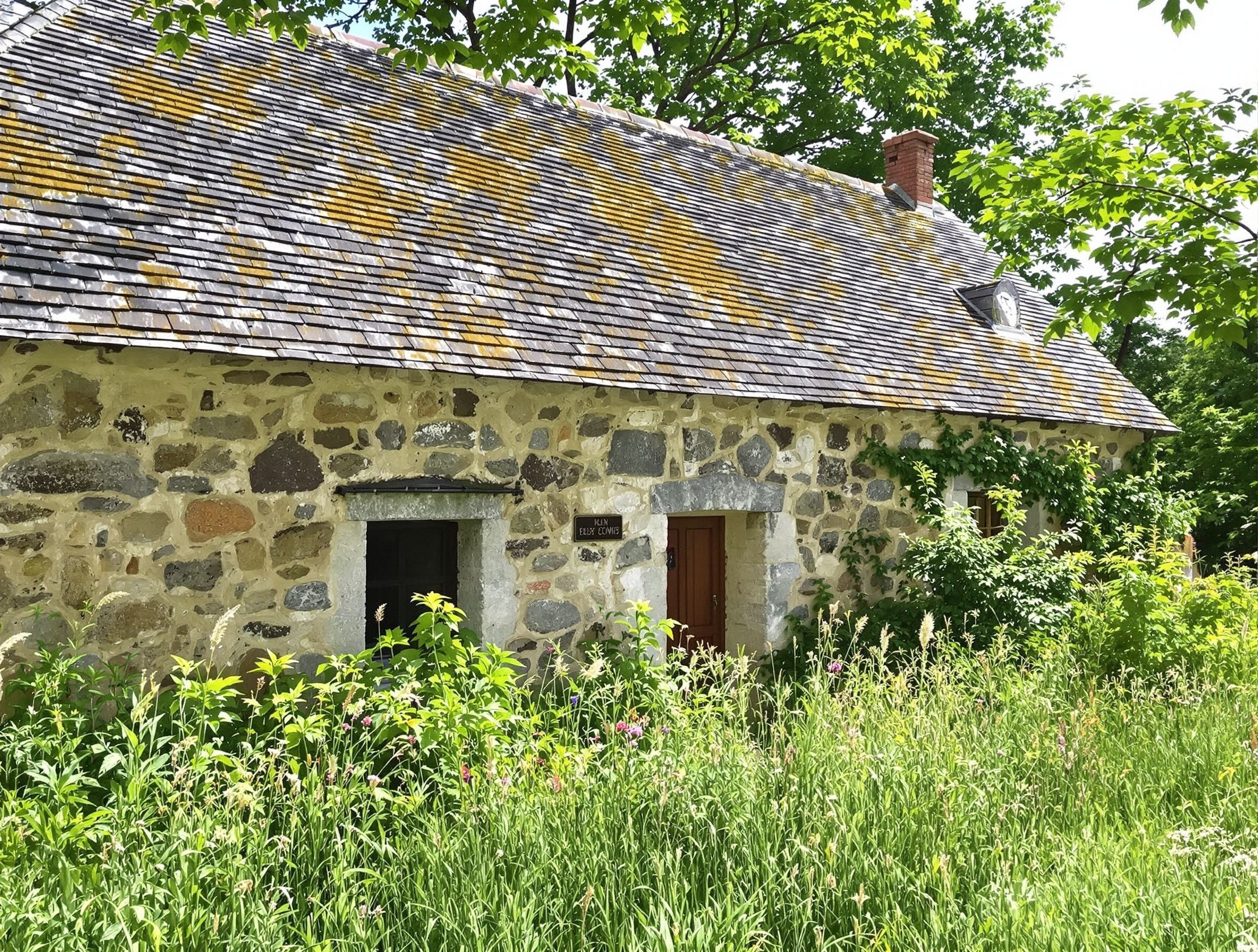 Vieille bâtisse en pierre typique du Cantal avec toit en lauze et jardin verdoyant